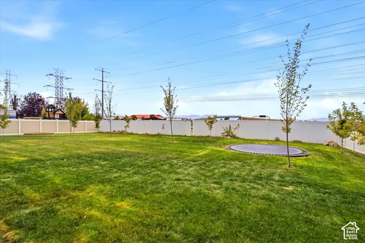 Expansive green lawn with a perimeter fence, dotted with young trees and a circular in-ground feature