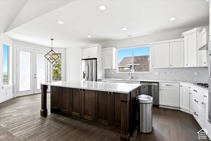 Kitchen featuring a large central island with a light-toned countertop, white cabinetry, stainless steel appliances, and wood-finish flooring