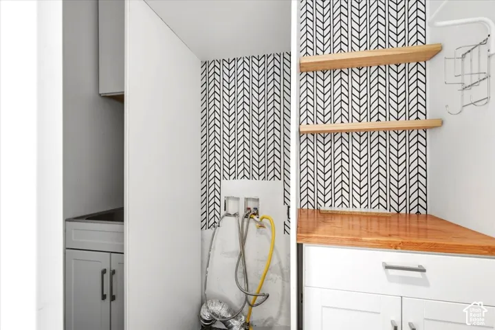 White cabinetry with wood-finish countertop, patterned accent wall, and open wood shelving