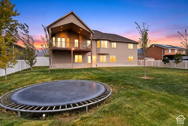 Spacious backyard featuring a manicured lawn, a two-story stucco exterior, a large upper-level balcony, and multiple windows