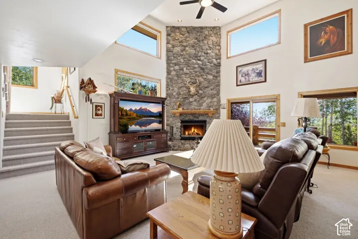 Great room with a soaring ceiling, stone-clad fireplace, large windows, and a ceiling fan
