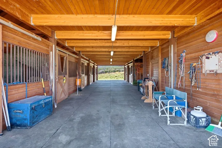 Wood-paneled barn with exposed wooden beams, concrete flooring, and multiple stalls with sliding wood doors