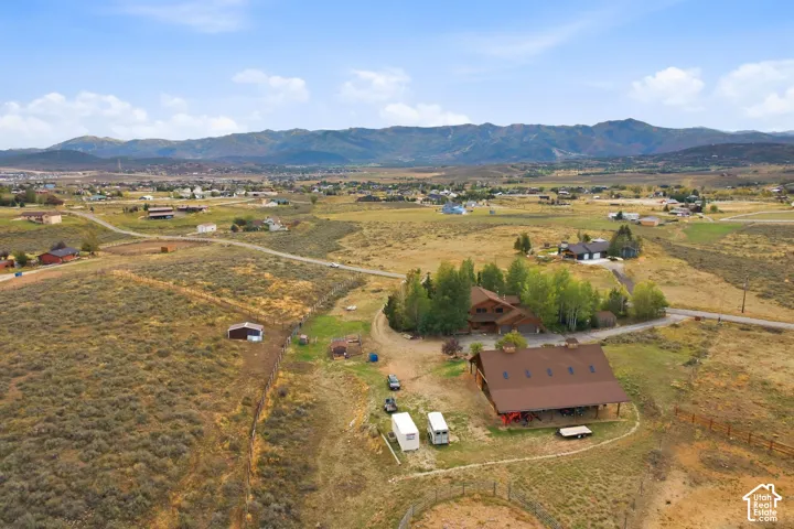 Expansive property with a mountain backdrop, featuring a primary residence with surrounding mature trees and an additional large structure with a covered porch