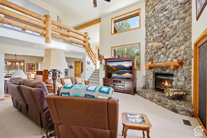 Two-story stone fireplace with log mantel, log railing overlooking the living space, vaulted ceilings, and high windows