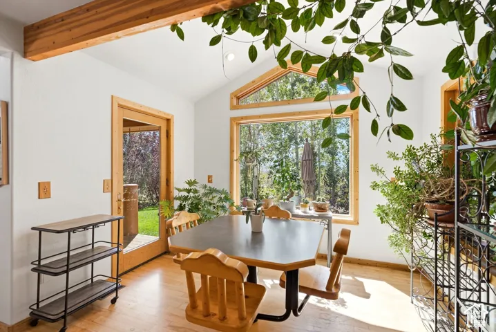 Vaulted ceiling with exposed wood beam, large picture window with transom, wood-finish flooring, and wood-framed exterior door