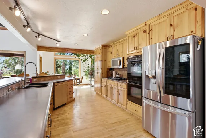 Kitchen featuring wood-finish cabinetry, stainless steel appliances, a built-in double oven, a workstation sink, and wood-finish flooring