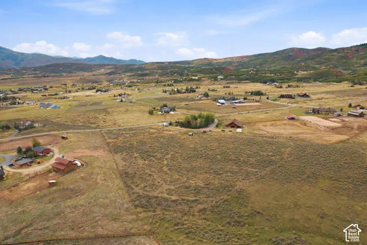 Expansive property featuring undeveloped land, scattered residential structures, and distant mountainous terrain