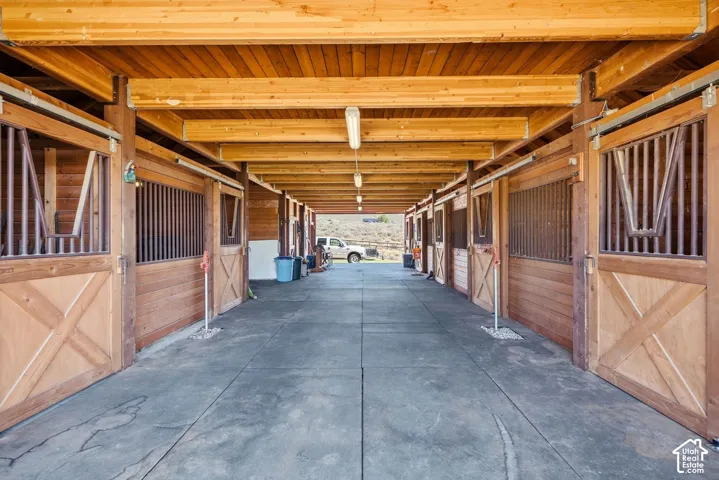 Covered walkway featuring multiple stalls with wood doors and metal grates, supported by substantial wood beams