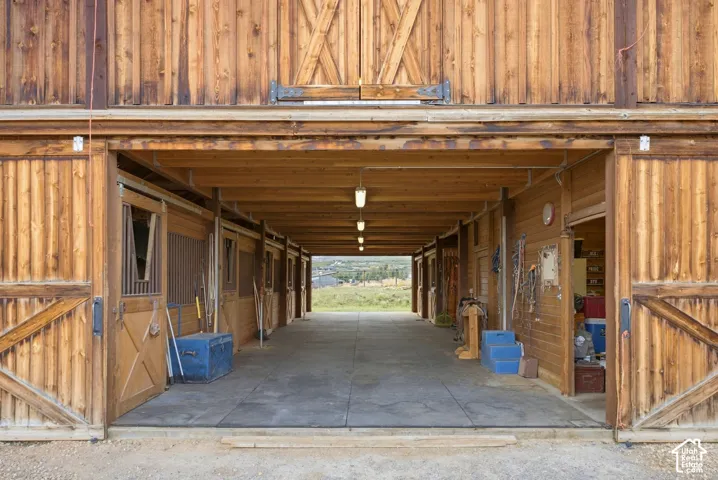 Wood-paneled barn exterior featuring multiple stalls with half-doors, a concrete walkway, and overhead lighting