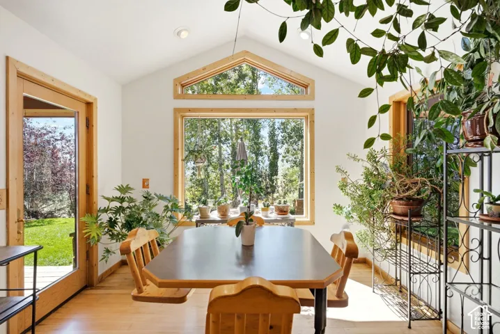 Vaulted ceiling with recessed lighting, wood-trim windows, light wood-finish flooring, and a glass-paneled door