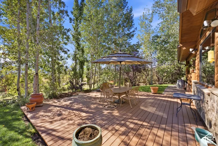 Expansive outdoor deck with wood-finish planks, surrounded by mature trees, and featuring a stone-clad exterior wall