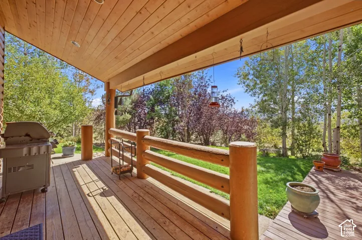 Covered outdoor deck with wood-finish flooring, log column supports, and a natural log railing