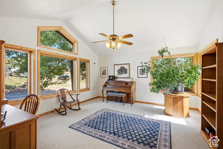 Vaulted ceiling with a ceiling fan, light-toned carpeting, and multiple windows with wood trim