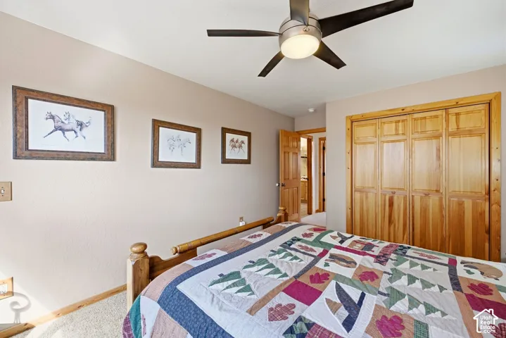 Integrated ceiling fan with light fixture, natural wood bifold closet doors, light-colored wall paint, and light-toned carpeting
