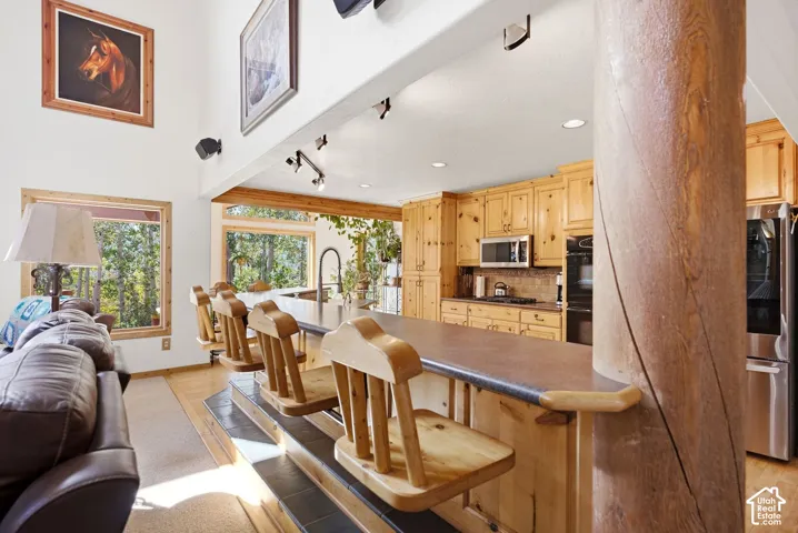 Kitchen featuring natural wood cabinetry, stainless steel appliances, a breakfast bar with seating, and a tile backsplash