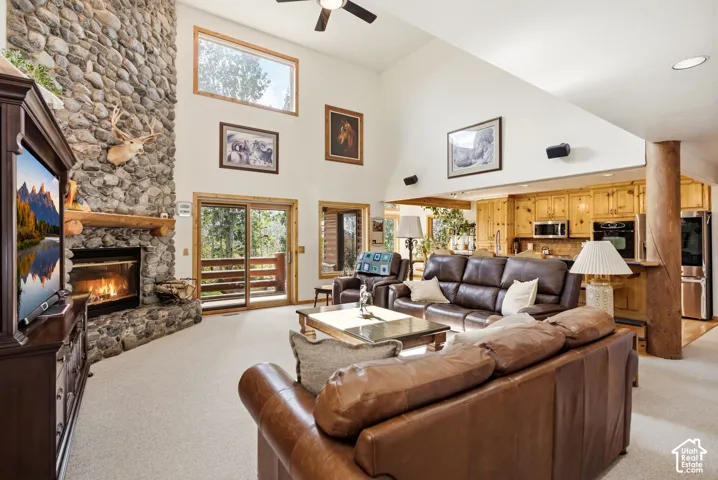 Vaulted ceilings with a ceiling fan, stone fireplace with a wood mantle, sliding glass door to a balcony, and wood-finish cabinetry