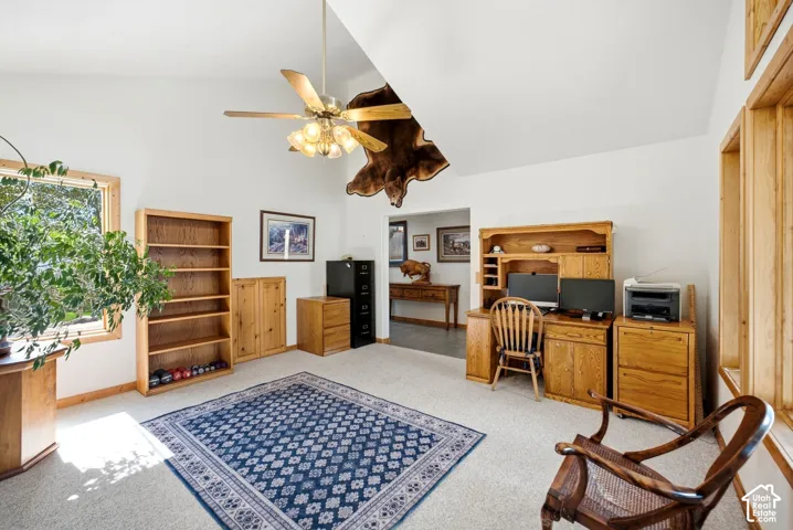 Vaulted ceiling with ceiling fan, large window with natural wood trim, built-in wooden shelving, and warm-toned carpeting