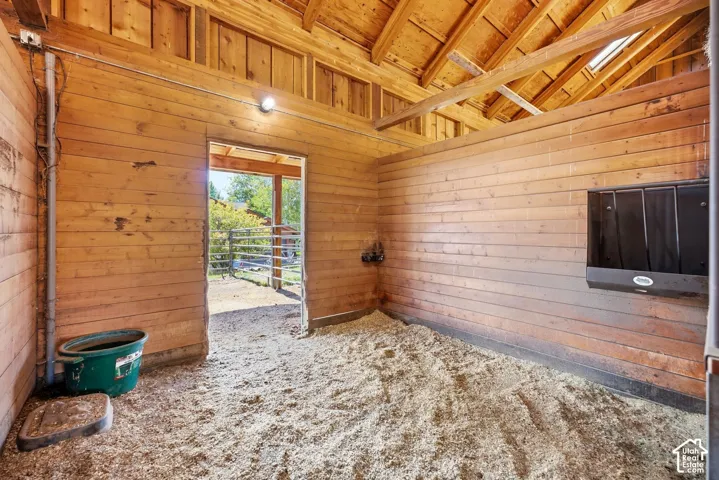 Wood-paneled interior walls, exposed wood beam ceiling, skylight, wall-mounted feeder, and an open doorway to an outdoor fenced area