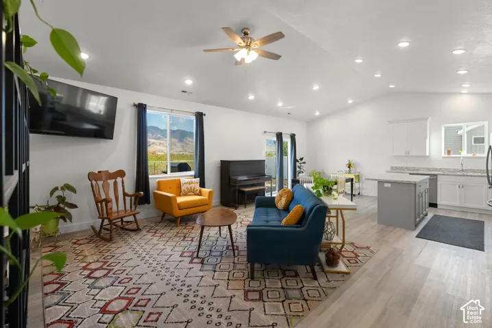 Open-concept living area featuring vaulted ceilings, recessed lighting, wood-finish flooring, and a kitchen with white cabinetry and an island