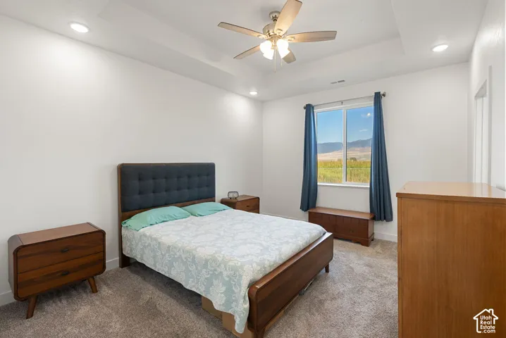 Tray ceiling with recessed lighting, ceiling fan, large window with expansive mountain scenery, and plush carpeting
