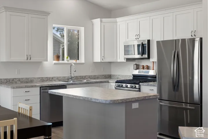 White shaker-style cabinetry, stainless steel appliances, a corner sink, an island with a breakfast bar, and light-toned countertops