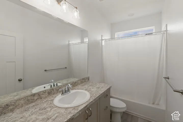 Bathroom featuring a vanity with a laminate countertop, an undermount sink, a shower-tub combination, a toilet, and wood-finish flooring