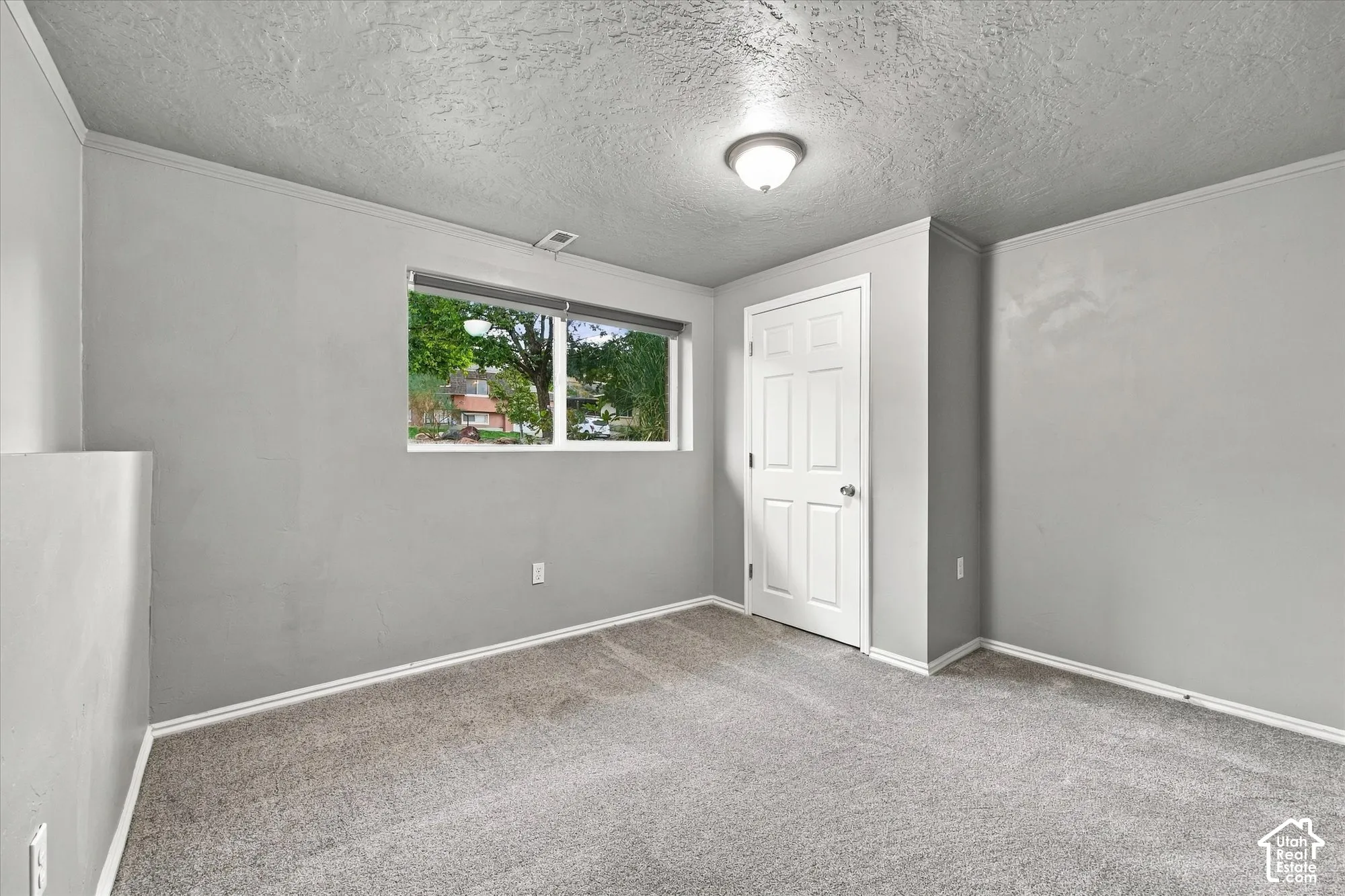 Gray-toned walls, textured ceiling, light gray carpeting, and a single window with a white frame