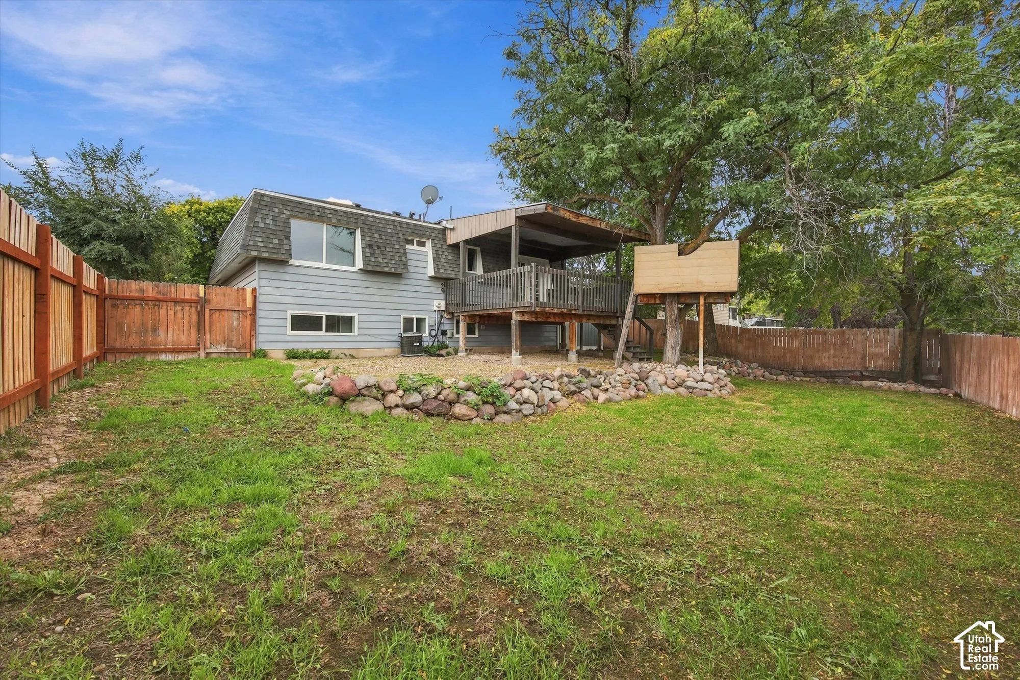 Expansive backyard with wood fencing, mature trees, and a raised deck
