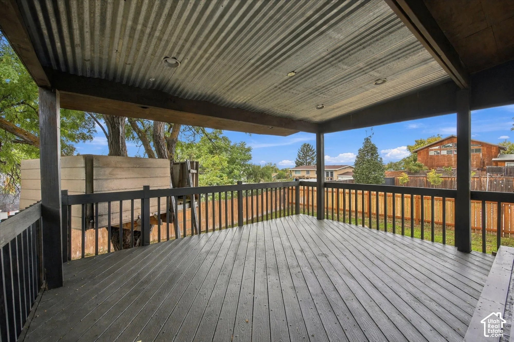 Covered outdoor deck featuring a corrugated metal ceiling, recessed lighting, wood-finish flooring, and dark-stained railings