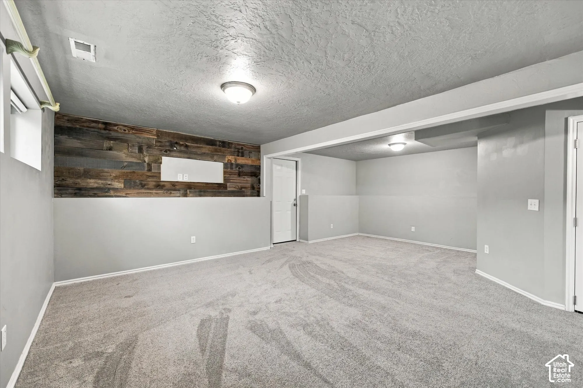 Recessed ceiling lighting, wood-finish accent wall, neutral tone carpeting, and painted drywall