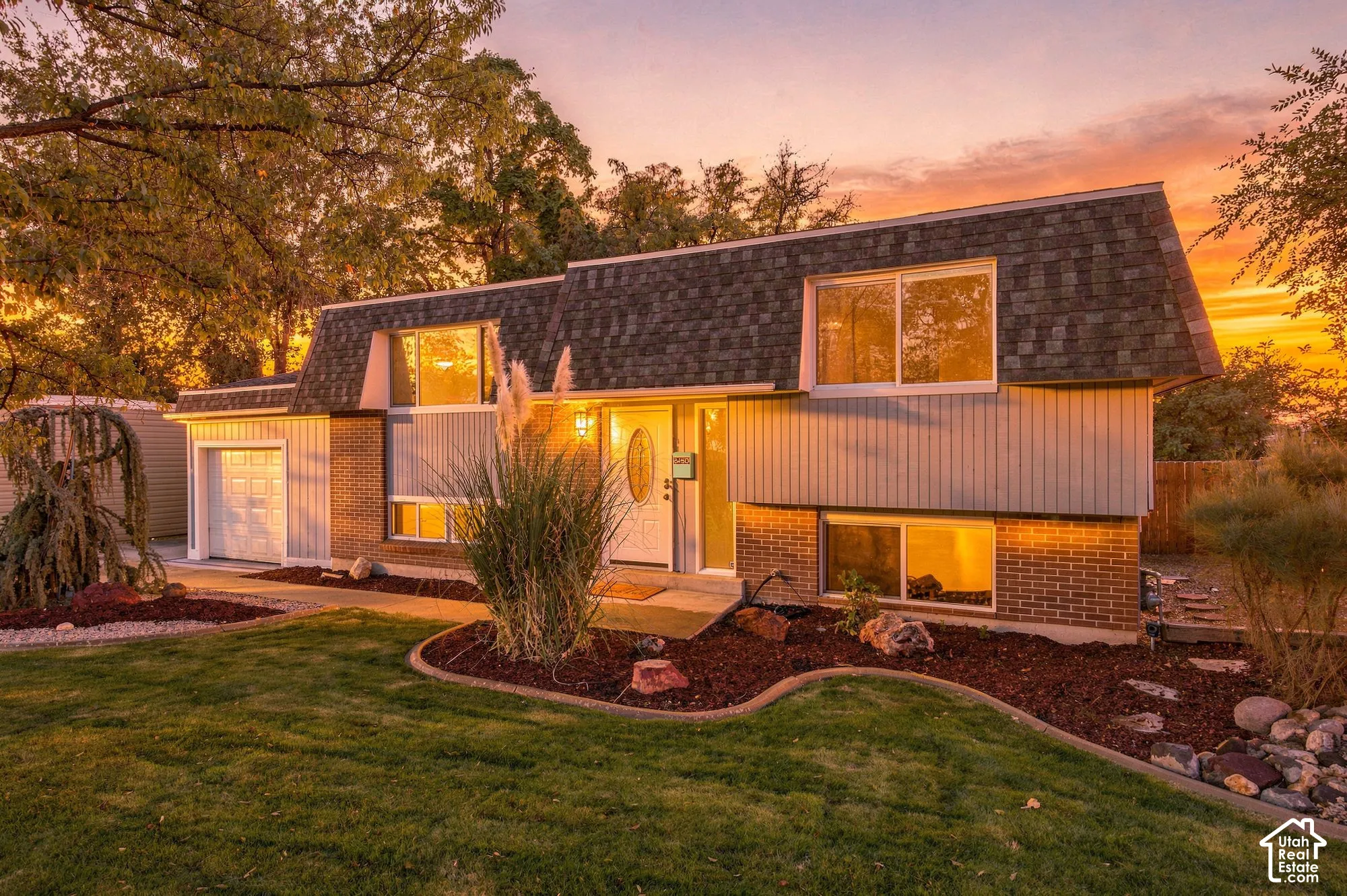 Split-level home featuring brick and vertical siding, a gambrel roof, an attached garage, and landscaped front yard