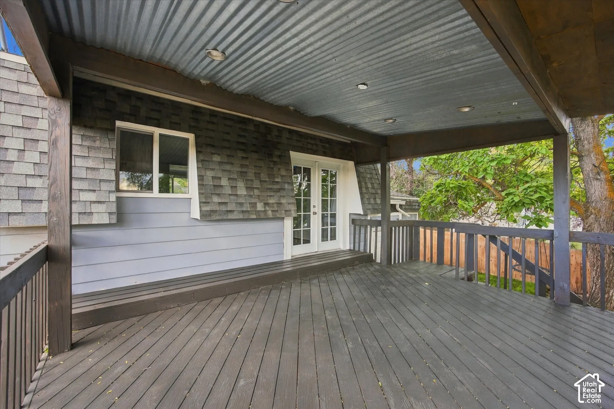 Expansive outdoor deck featuring wood-finish flooring, a wood-finish railing, and a corrugated metal ceiling with recessed lighting