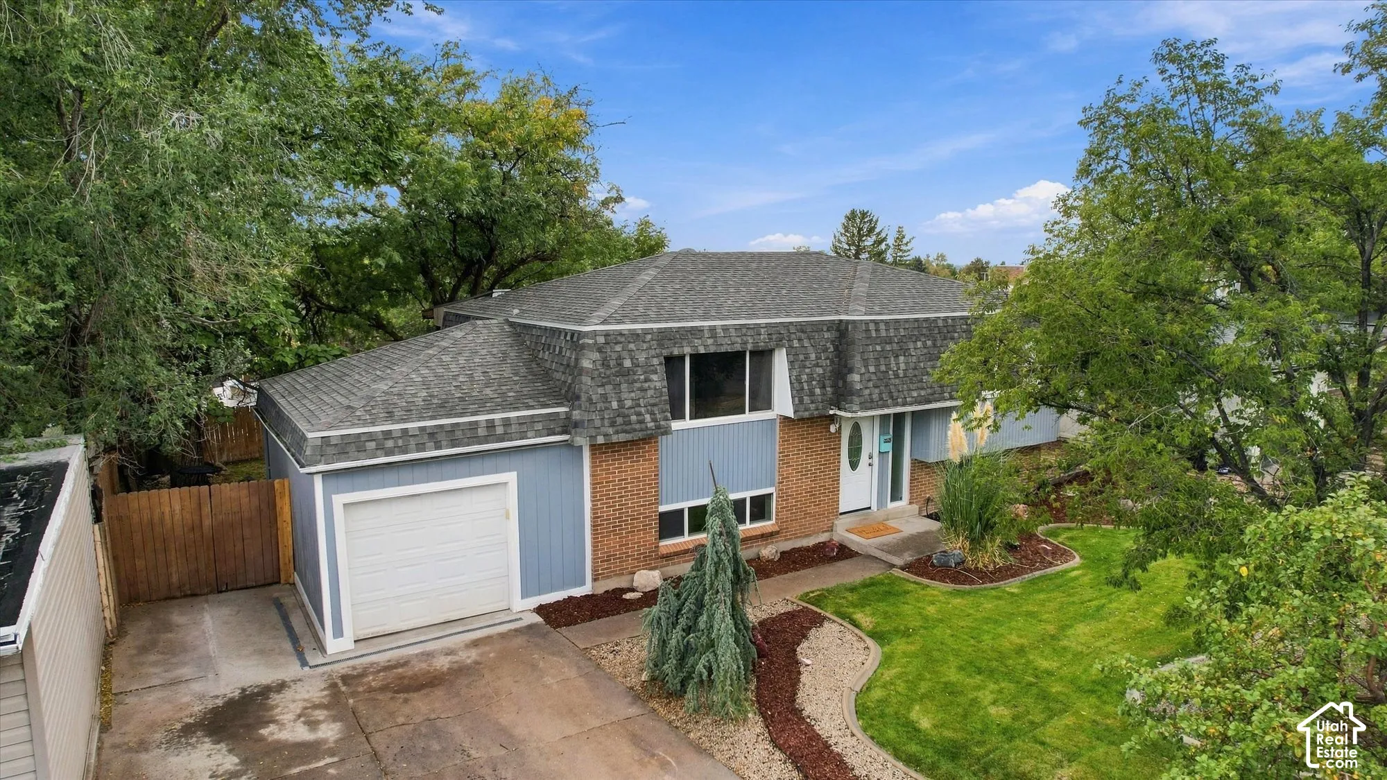Split-level residence featuring brick and siding exterior, attached garage, and a landscaped front yard with mature trees
