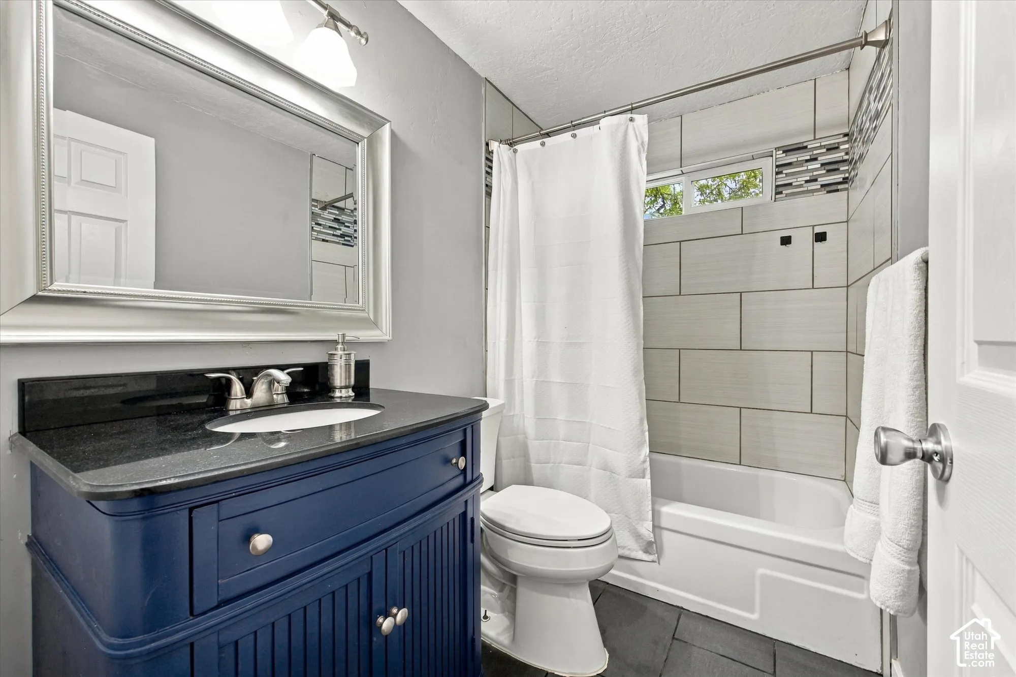 Bathroom featuring a blue wood-finish vanity with a dark countertop, an undermount sink, a large framed mirror, and a tiled shower with a decorative accent band