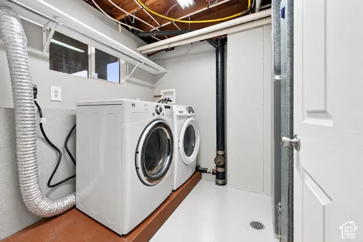 Utility area featuring a painted concrete floor, dedicated laundry hookups, a floor drain, a horizontal window, and an elevated wood-finish platform