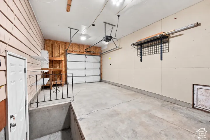 Enclosed garage featuring a white sectional overhead door with auto opener, built-in wall shelving, integrated metal storage rack, saftey railing