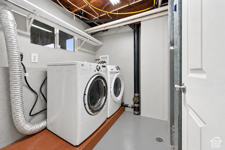 Utility area featuring a raised wood-finish platform, concrete flooring, sliding window, and exposed ceiling joists