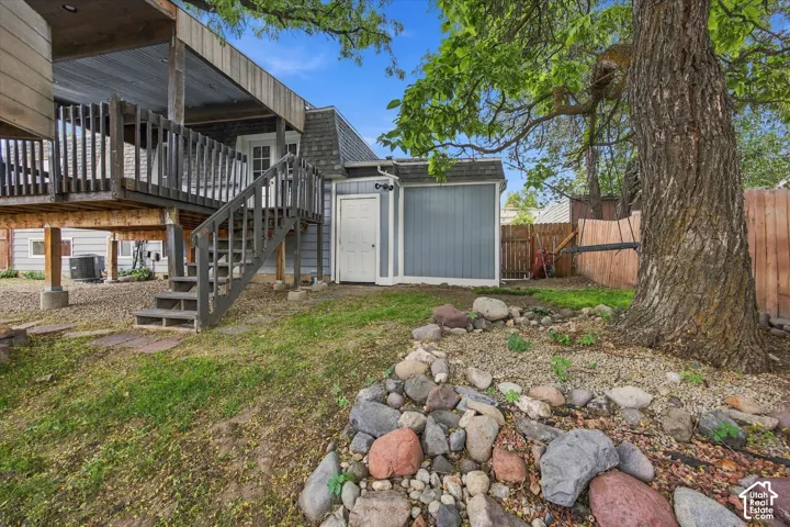 Spacious backyard retreat featuring mature shade trees, natural stone landscaping, and a detached storage shed with gray composite siding