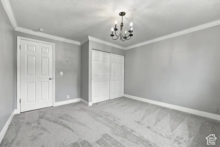 Crown molding, carpeted flooring, paneled interior door, bi-fold closet doors, and a chandelier lighting fixture