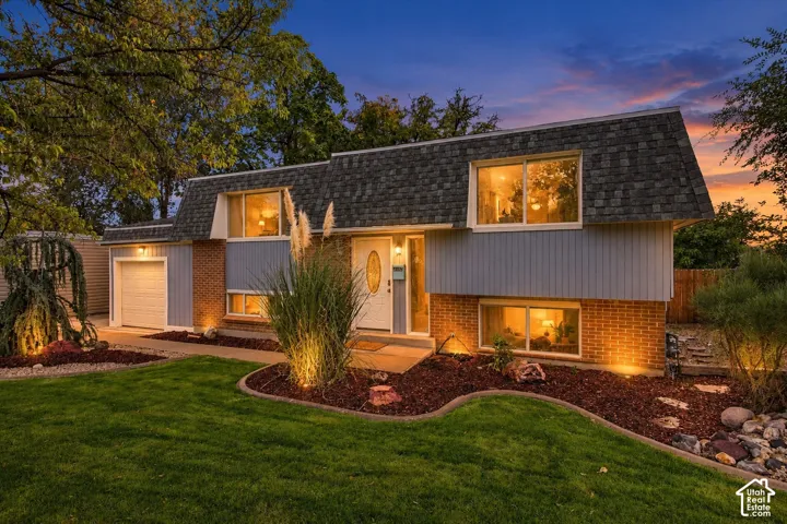 Split-level exterior featuring a combination of brick and vertical siding, a mansard-style roof, single-car garage, and manicured landscaping