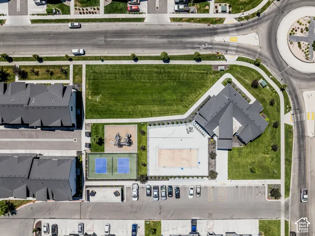 Aerial view showcasing a modern residence with a spacious backyard featuring manicured lawn, hardscape patio, and recreational amenities including a volleyball court and basketball court