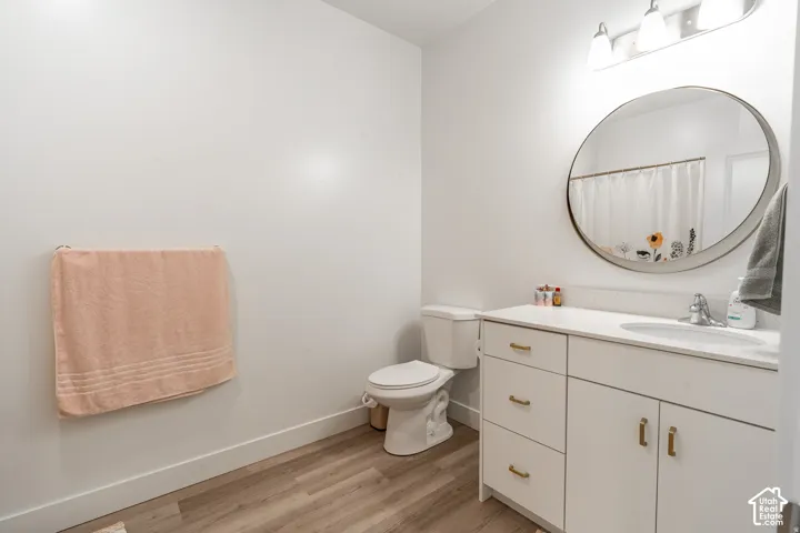 Spa-inspired bathroom featuring a white vanity with ample storage, wood-finish flooring, a circular framed mirror, and chrome fixtures
