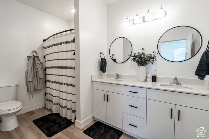 Modern primary bathroom featuring dual round mirrors with integrated lighting, a white vanity with multiple drawers and cabinet storage, quartz countertop with dual sinks, and wood-finish flooring