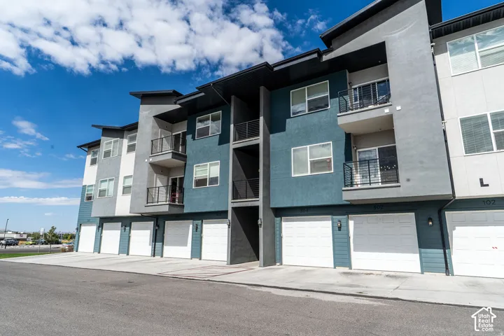 Multi-story building with textured facade, private balconies, individual garages, and integrated exterior lighting