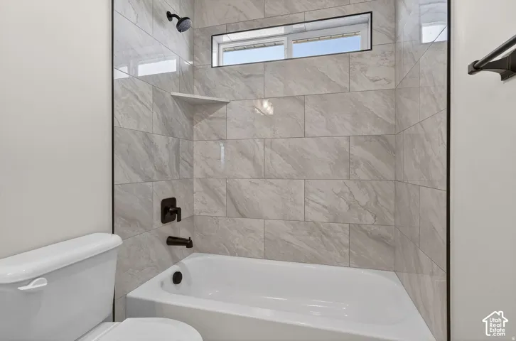 Bathtub with dark bronze fixtures, tiled shower surround, recessed shelf, and horizontal privacy window