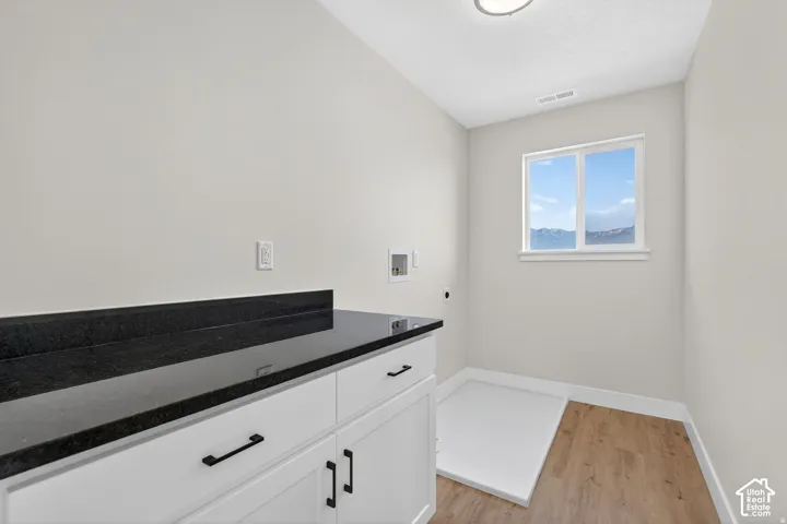 White cabinetry with black hardware, dark countertop, and wood-finish flooring
