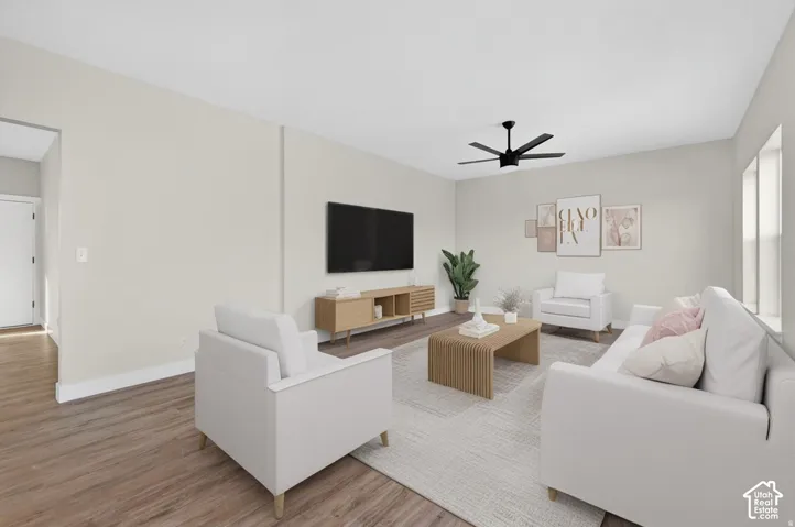 Recessed wall-mounted television, wood-finish flooring, white baseboards, light-toned walls, and a black ceiling fan