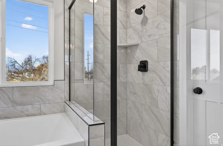 Shower with matte black fixtures, integrated shelving, and white hexagonal tile flooring