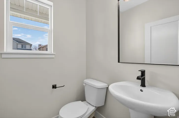 White pedestal sink with a matte black faucet, wall-mounted rectangular mirror, and a white toilet