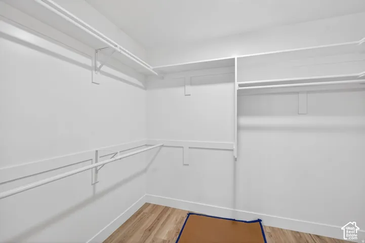 Walk-in closet with ample storage, white shelving, and wood-finish flooring